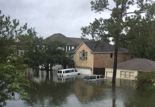 Flooded residential area with water surrounding houses and vehicles.