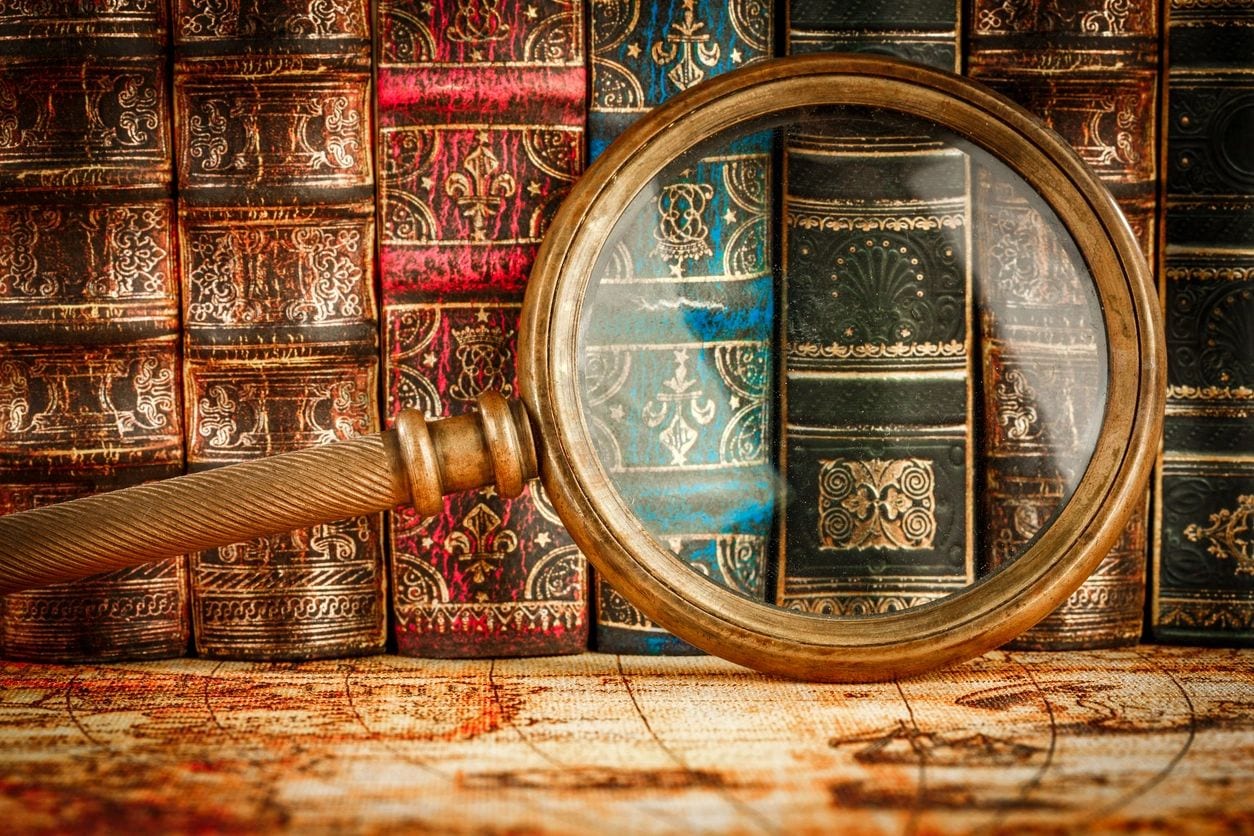 Magnifying glass over old leather-bound books showing detailed textures.