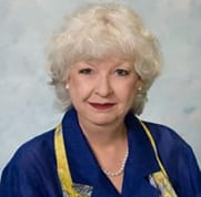 Portrait of an elderly woman with curly white hair and a blue outfit.