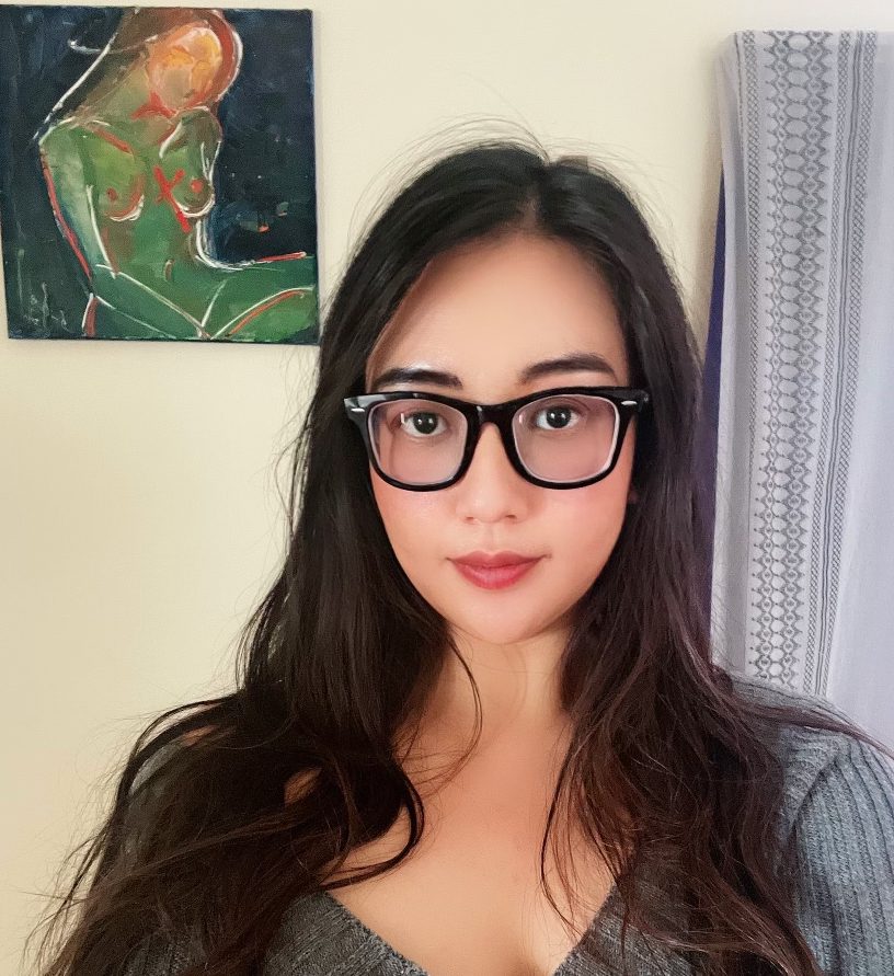 A young woman with long dark hair wearing glasses and a gray top.